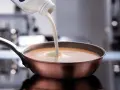 Sahne wird in eine Pfanne mit einer cremigen Sauce gegossen. Perfekt, welche Sahne zum Kochen für eine köstliche Mahlzeit.