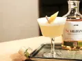 Ein erfrischender Sour Cocktail mit Zitronenspalte, neben einer Flasche Schlitzer Single Grain Whisky. Perfekt für ein Sour Cocktail Rezept.
