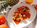 Leckeres Currywurst Rezept: Geschnittene Wurst in würziger Sauce, garniert mit Petersilie. Daneben Ananas, Orange und Tomaten.