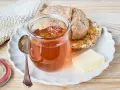 Glas mit goldbraunem Apfelgelee aus Apfelsaft, daneben ein Stück Butter und ein halbes Brot auf einem Teller.