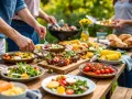 Leckere Beilagen zum Grillen: Salate, Maiskolben, Tomaten und Spieße auf einem Holztisch im Freien.