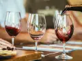 Rotwein wird in ein Glas gegossen, der Duft von **Wein** und **Tanninen** liegt in der Luft. Daneben ein leeres Glas und ein Teller mit Käse und Crackern.