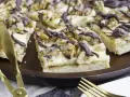 Ein "friss dich dumm kuchen" mit cremiger Füllung, Walnüssen und Schokoladendrizzle auf einem Holztablett. Goldene Gabeln liegen bereit.