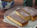 Drei rechteckige Stücke mandelkuchen vom blech, mit Puderzucker bestäubt, auf einem Glas-Teller.