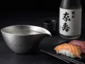 Sake-Flasche und eine Kanne mit Sake, die klassische Getränke, was trinkt man zu Sushi. Sushi-Stücke liegen daneben.