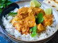 Ein köstliches indisches Curry mit zarten Hähnchenstücken in cremiger Sauce, serviert auf lockerem Reis, garniert mit frischer Petersilie und Limettenspalten.