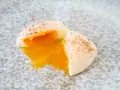 Ein perfekt pochiertes Ei mit flüssigem Eigelb, bestreut mit schwarzem Pfeffer, auf einem gesprenkelten Teller.