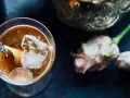 Ein erfrischender Gin Tee mit Eis, Zitrone und Lavendelblüten. Daneben zarte Rosen und eine verzierte Karaffe.