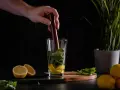 Ein Barkeeper bereitet einen erfrischenden Cocktail mit Basilikum und Gin zu, indem er die Zutaten im Glas zerdrückt.