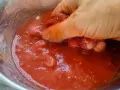 Hand zerdrückt Tomaten in einer Schüssel. So einfach lässt sich Tomatensauce selber machen.