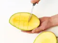 Eine Hand schneidet mit einem Messer eine reife Mango in Würfel. So einfach lässt sich die Frucht für den Verzehr vorbereiten.