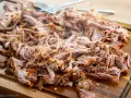 Saftiges pulled pork, zart zerfallen, liegt auf einem Holzbrett. Eine Gabel liegt bereit, um das Fleisch zu servieren.