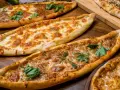 Mehrere Pide-Gerichte, darunter eines mit Käse und eines mit Hackfleisch, sind auf einem Holztisch arrangiert. Ein köstliches Pide Rezept!