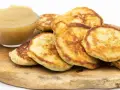 Goldbraune Quarkkeulchen ohne Kartoffeln, serviert mit Apfelmus auf einem Holzbrett.