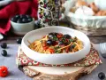 Eine Schüssel Spaghetti Puttanesca, garniert mit schwarzen Oliven und Kräutern, auf einem rustikalen Holzständer.