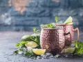 Zwei eisgekühlte Kupferbecher mit einem erfrischenden alkoholfreien Ginger Beer Cocktail, garniert mit Limette und Minze.