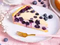 Ein Stück saftiger Heidelbeerkuchen Landfrauenart auf einem Teller, garniert mit frischen Beeren und einer Gabel.