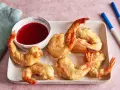 Knusprige tempura garnelen auf einem Teller mit süß-saurer Sauce und Stäbchen.