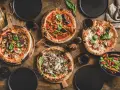 Vier leckere Pizzen und ein Salat auf Holztisch. Die Frage welcher Wein zu Pizza passt, wird hier mit Rotwein beantwortet.