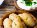Kleine, gekochte Kartoffeln mit Kümmel in einer Holzschale, daneben eine Schale mit Quark und Kräutern. Ein rustikales Gericht: Kartoffeln mit Quark.