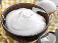 Perfekt geschlagener Eischnee in einer Schüssel, bereit für süße Kreationen. Daneben liegen Eier und ein Schneebesen.