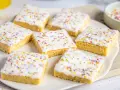 Sieben quadratische Kuchenstücke mit weißer Glasur und bunten Streuseln, perfekt für ein schnelles Fantakuchen Tassenrezept.