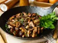 Gebratene Champignons in einer Pfanne, garniert mit frischer Petersilie. Köstlich und einfach zuzubereiten.