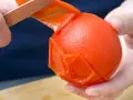 Hände ziehen mit einem Messer die Haut von einer Tomate ab. Die Tomate ist fast komplett geschält.