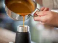 Eine orangefarbene Flüssigkeit wird aus einem Topf in ein schwarzes Gefäß gegossen. Ist das eine Espuma?