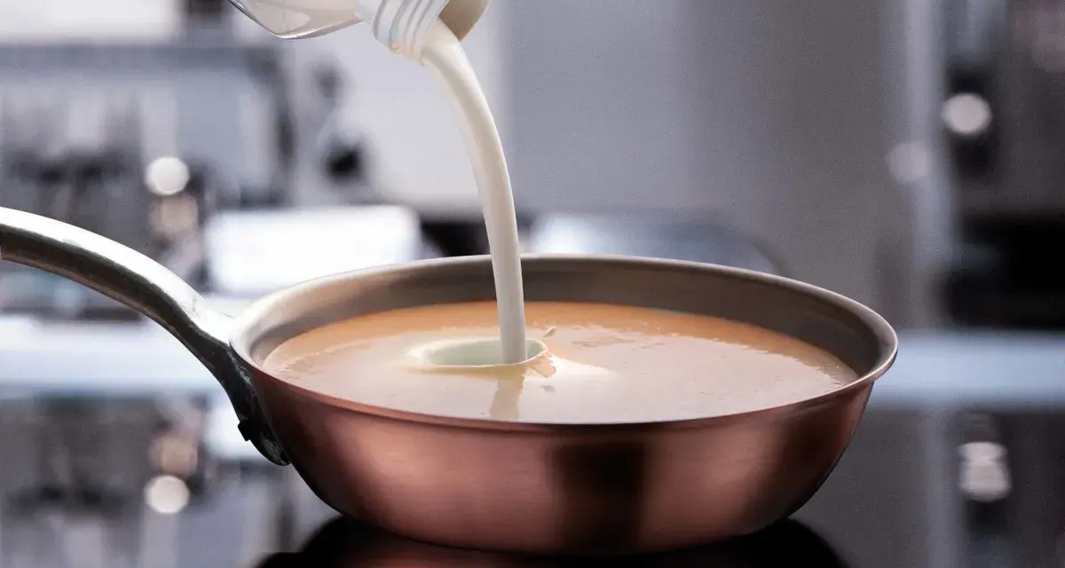 Sahne wird in eine Pfanne mit einer cremigen Sauce gegossen. Perfekt, welche Sahne zum Kochen für eine köstliche Mahlzeit.
