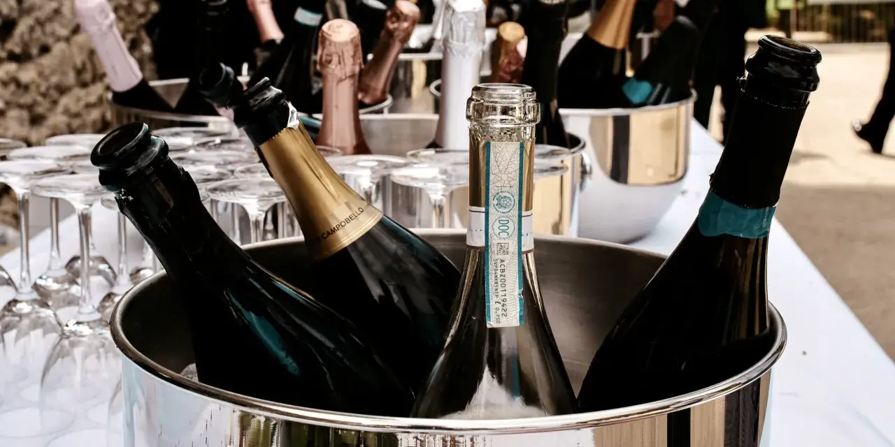 Mehrere Flaschen Sekt in einem silbernen Eiskübel, bereit für die Feier. Gläser stehen daneben.