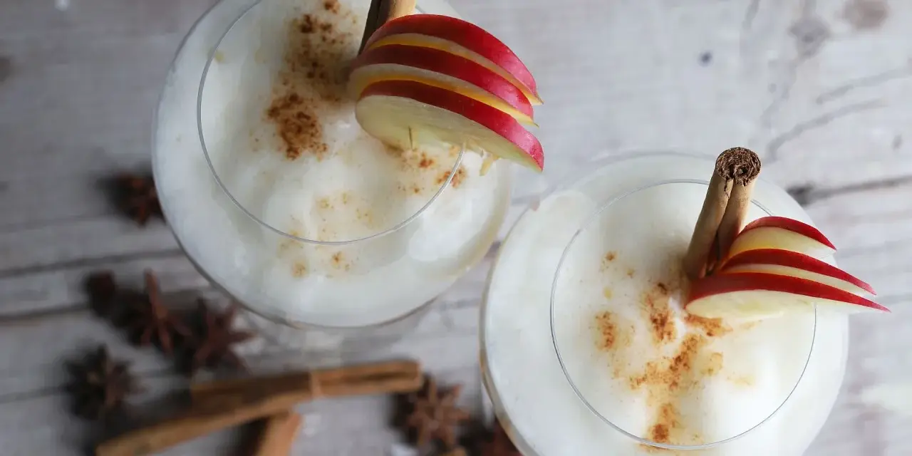 Zwei cremige Wintercocktails mit Zimt, Apfelscheiben und Sternanis.