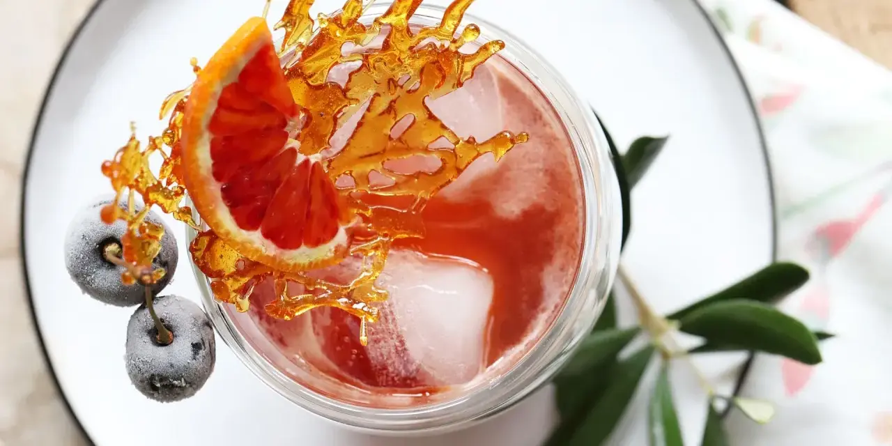 Ein erfrischender Sling Cocktail mit Blutorange, gefrorenen Beeren und Karamell-Dekoration.