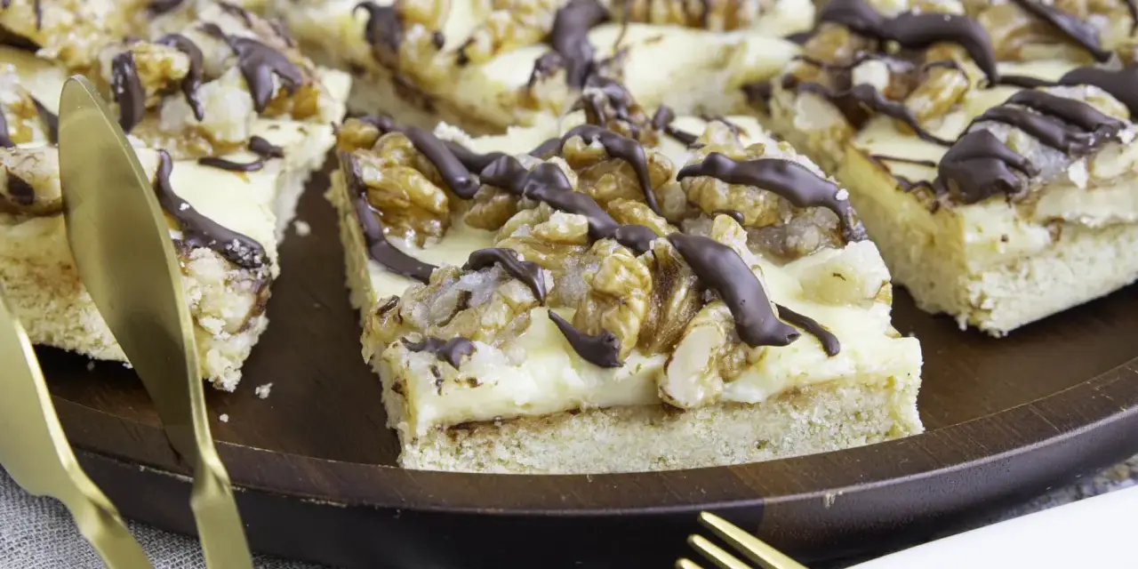 Ein "friss dich dumm kuchen" mit cremiger Füllung, Walnüssen und Schokoladendrizzle auf einem Holztablett. Goldene Gabeln liegen bereit.