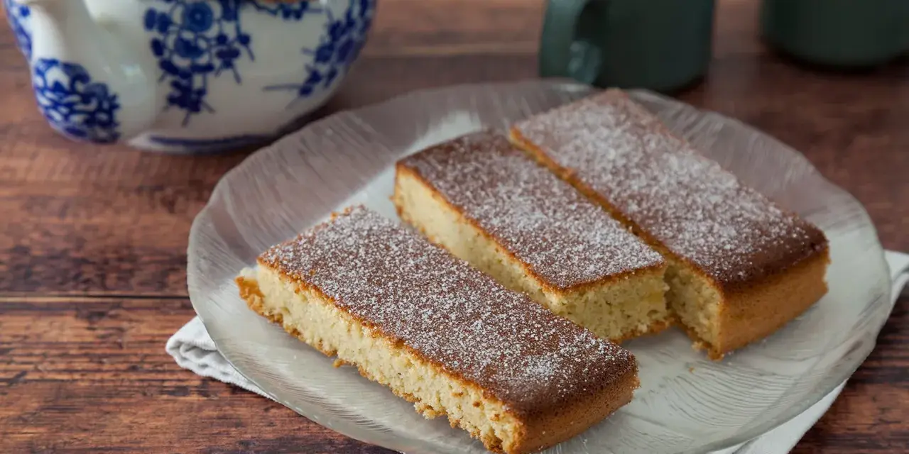 Drei rechteckige Stücke mandelkuchen vom blech, mit Puderzucker bestäubt, auf einem Glas-Teller.