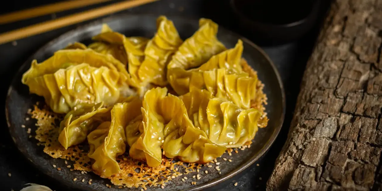 Goldbraune Gyoza auf knusprigem Sesam-Bett, bereit für ein köstliches Dumplings-Rezept. Dazu Sojasauce und Ingwer.
