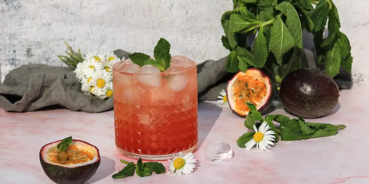 Erfrischender sanbitter cocktail mit Passionsfrucht, Minze und Eiswürfeln, garniert mit Gänseblümchen.