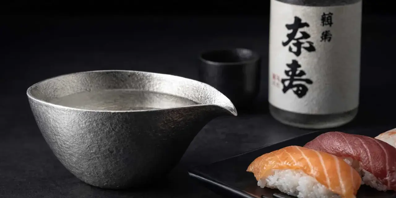 Sake-Flasche und eine Kanne mit Sake, die klassische Getränke, was trinkt man zu Sushi. Sushi-Stücke liegen daneben.