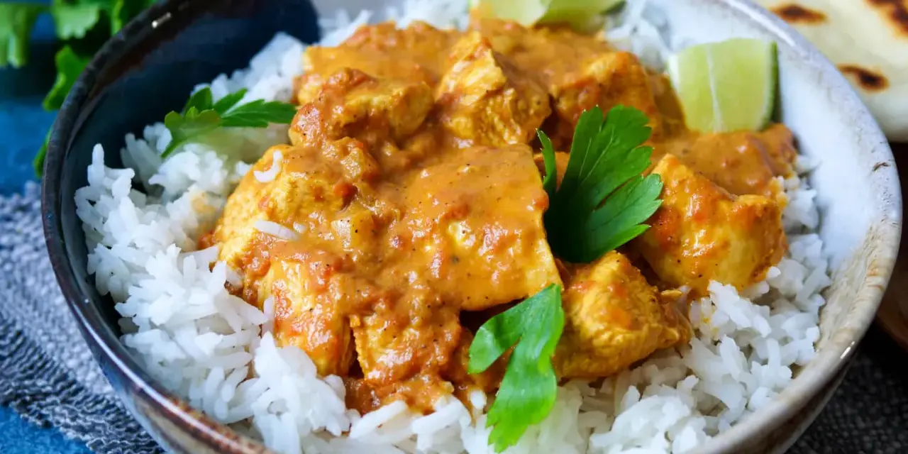 Ein köstliches indisches Curry mit zarten Hähnchenstücken in cremiger Sauce, serviert auf lockerem Reis, garniert mit frischer Petersilie und Limettenspalten.
