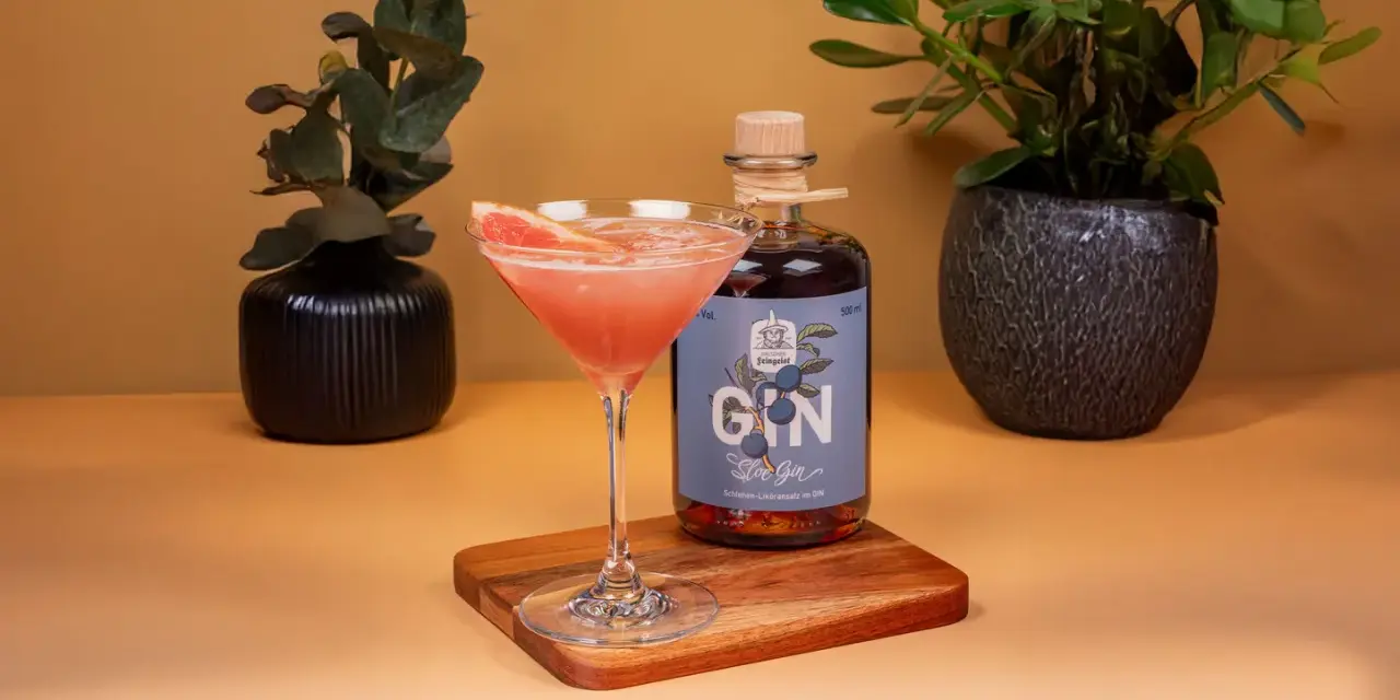 Ein erfrischender Sloe Gin Fizz mit Grapefruit-Garnitur neben einer Flasche Sloe Gin.