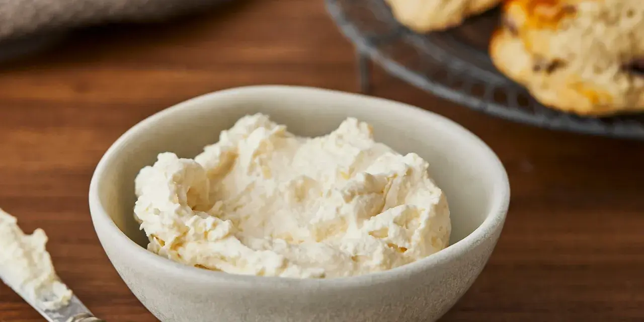 Cremiger Aufstrich in einer Schale, bereit für das perfekte Scones Rezept. Daneben ein Messer mit etwas Aufstrich.