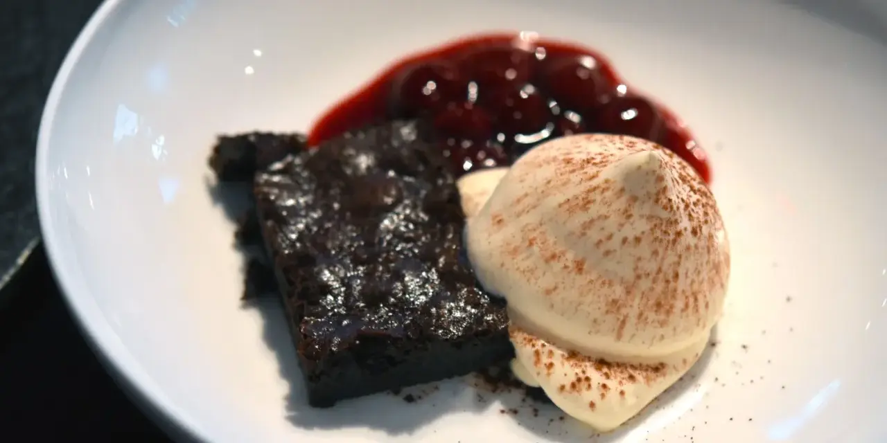 Schokoladenbrownie mit Fruchtsauce und einer perfekt hergestellten, luftigen Espuma, bestäubt mit Kakao.