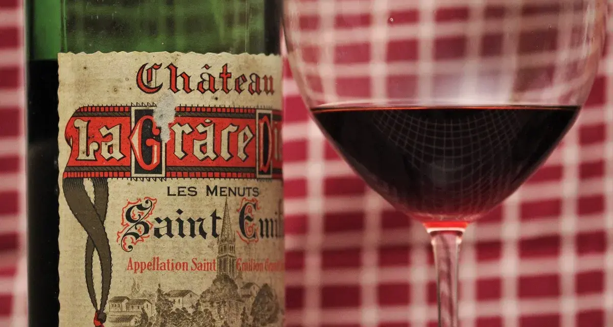 Ein Glas Rotwein neben einer Flasche Château La Grace Dieu. Die Bedeutung von "Grand Cru" auf dem Etikett deutet auf höchste Qualität hin.