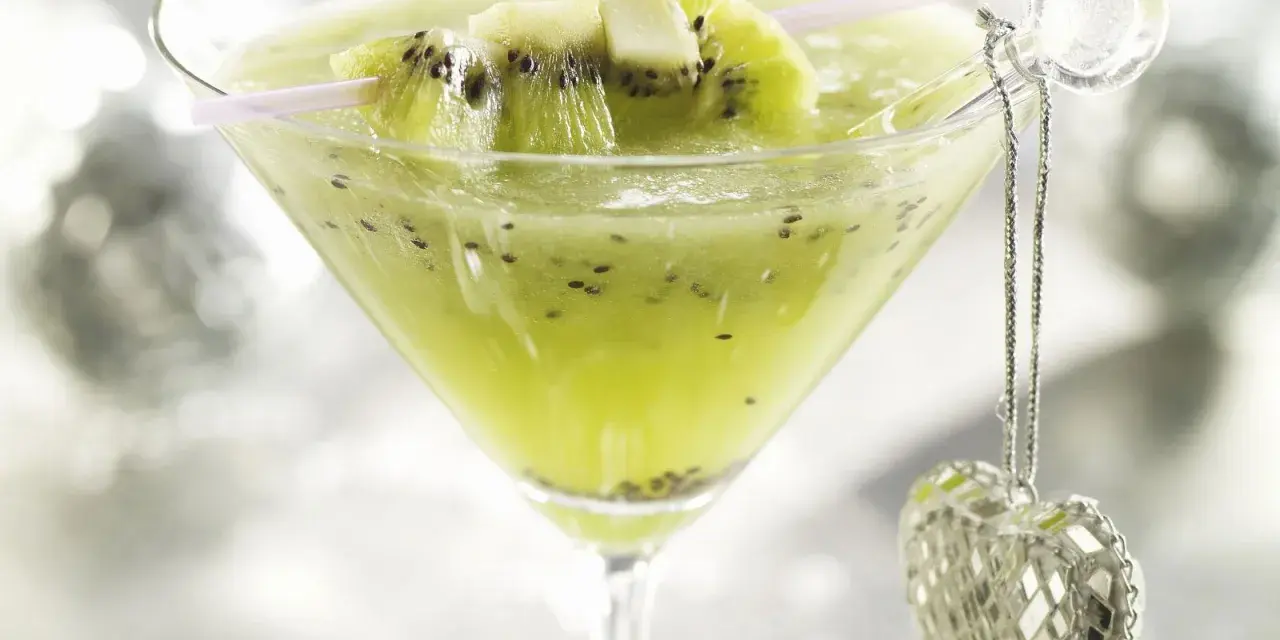 Erfrischender Kiwi-Cocktail im Martiniglas, garniert mit frischen Kiwischeiben und einem glitzernden Herz-Anhänger.