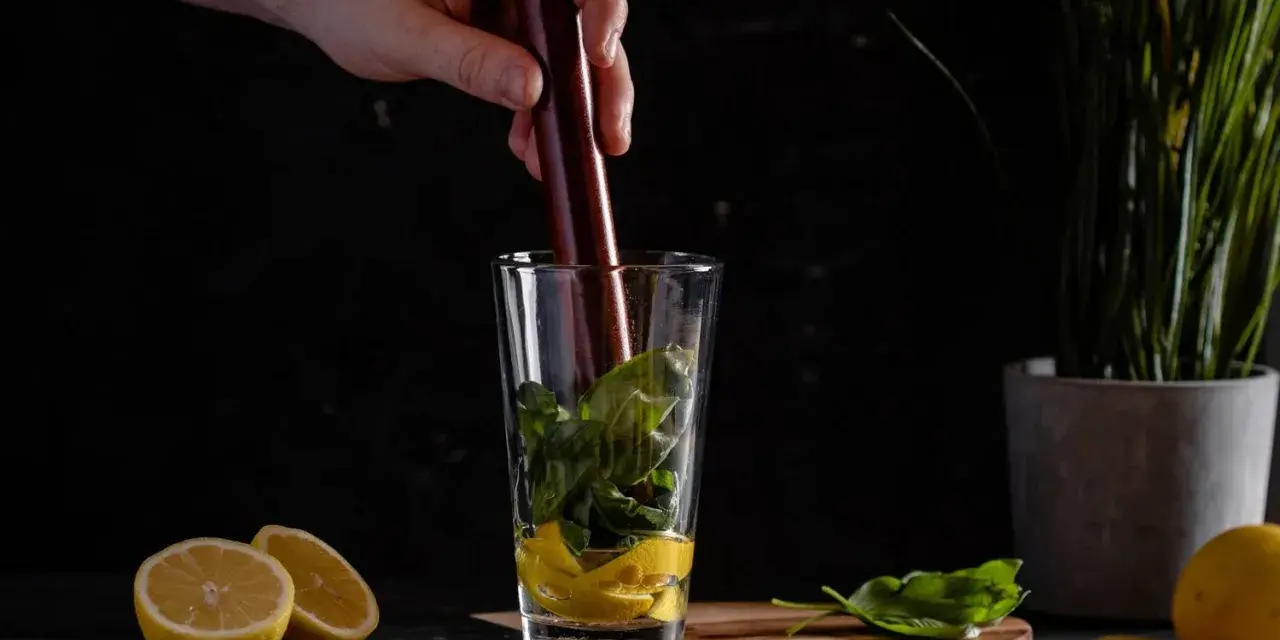 Ein Barkeeper bereitet einen erfrischenden Cocktail mit Basilikum und Gin zu, indem er die Zutaten im Glas zerdrückt.