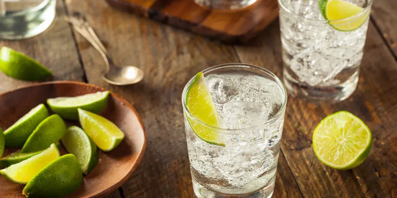 Erfrischender Jean Tonic mit Eis und Limettenspalten auf rustikalem Holztisch.