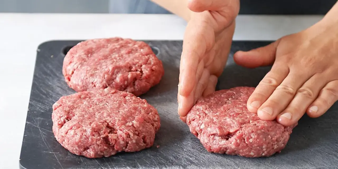 Hände formen rohe Burger-Patties auf einem dunklen Schneidebrett.
