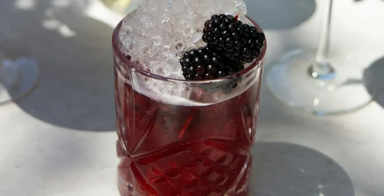 Ein Glas mit einem tiefroten Drink, gefüllt mit zerstoßenem Eis und garniert mit Brombeeren. Perfekt für die besten Cocktails an einem sonnigen Tag.