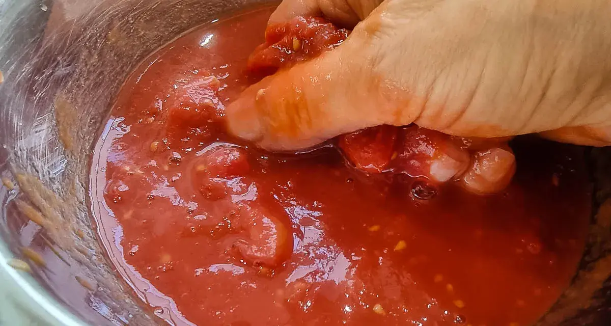 Hand zerdrückt Tomaten in einer Schüssel. So einfach lässt sich Tomatensauce selber machen.