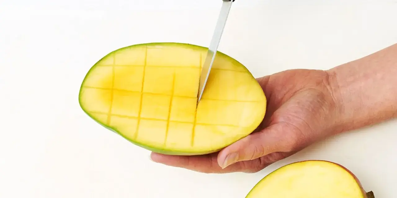 Eine Hand schneidet mit einem Messer eine reife Mango in Würfel. So einfach lässt sich die Frucht für den Verzehr vorbereiten.